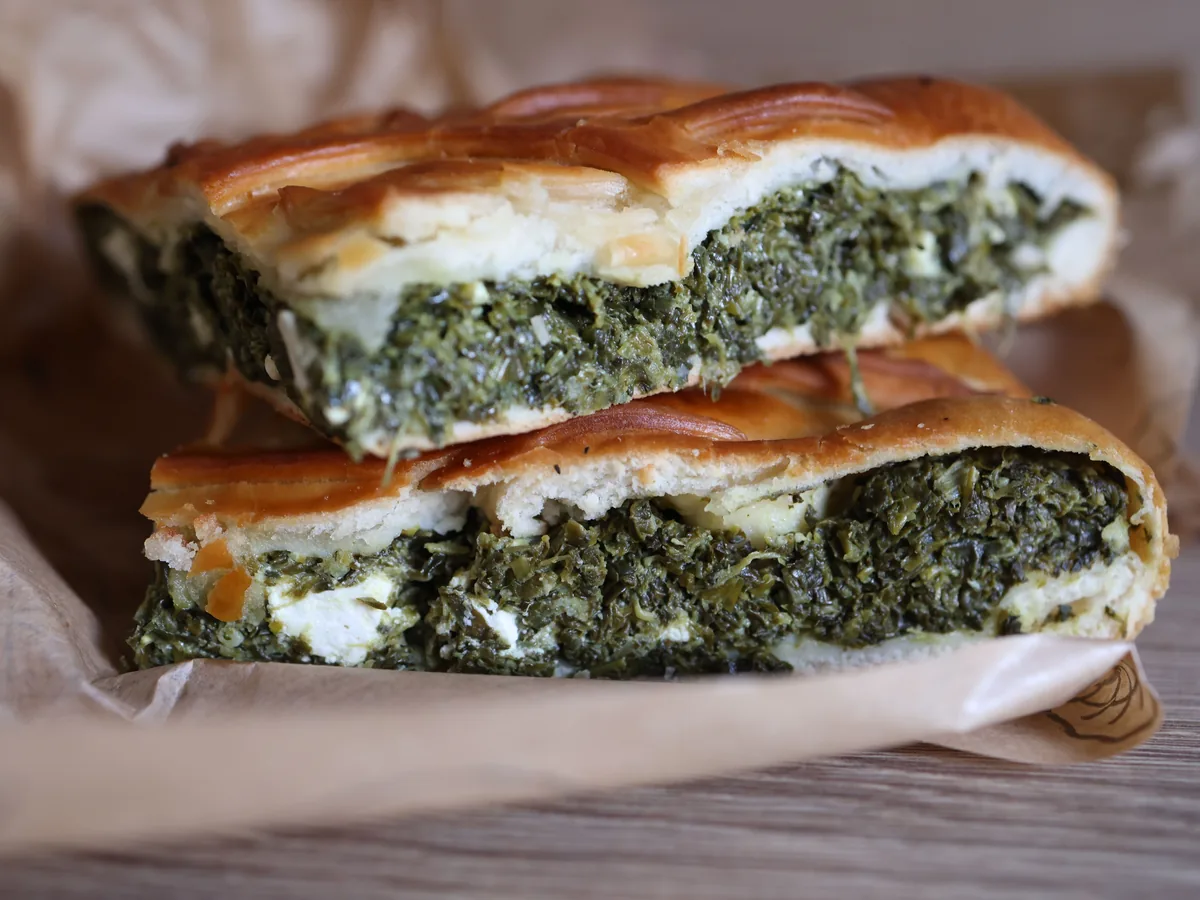 Two slices of spinach pie cut open to show a dark green filling with white feta between layers of golden filo pastry